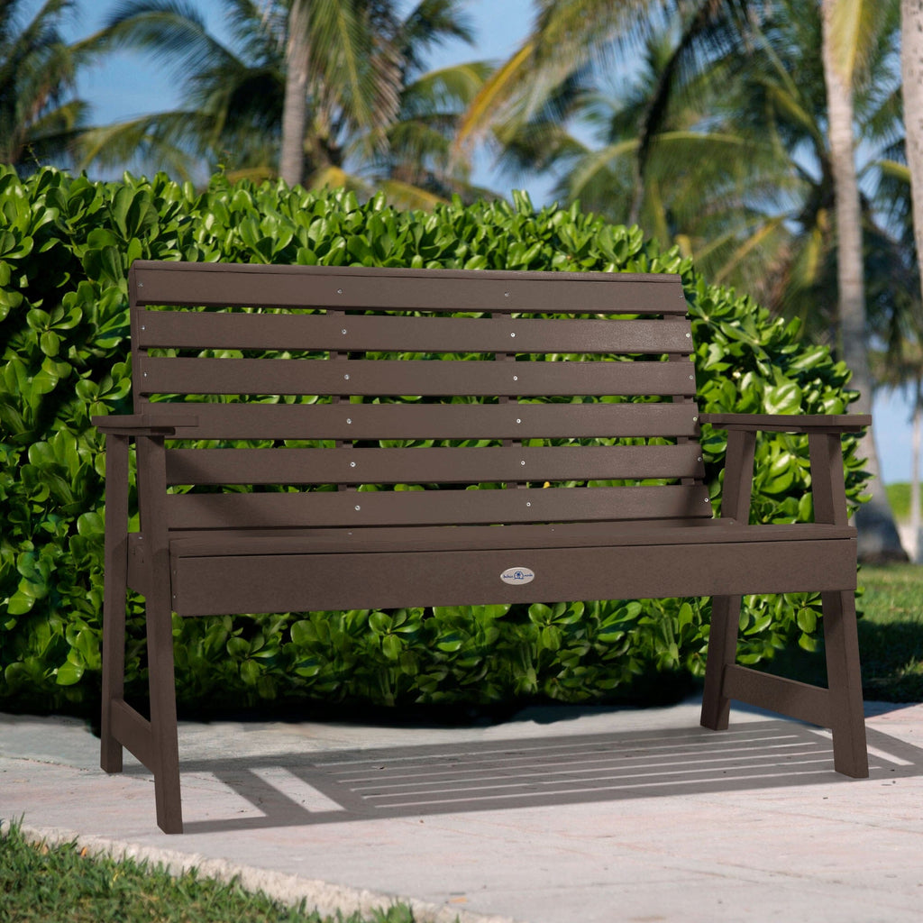 4ft Brown Riverside garden bench with palm tree and bush background   